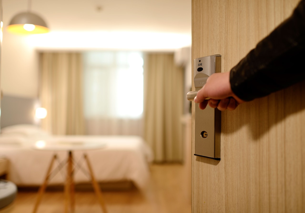 A hand opening a hotel room door with the room interior in the background