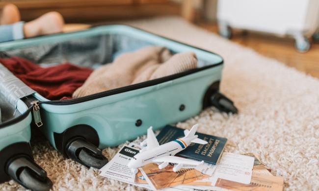 A suitcase open at home being packed with travel documents nearby
