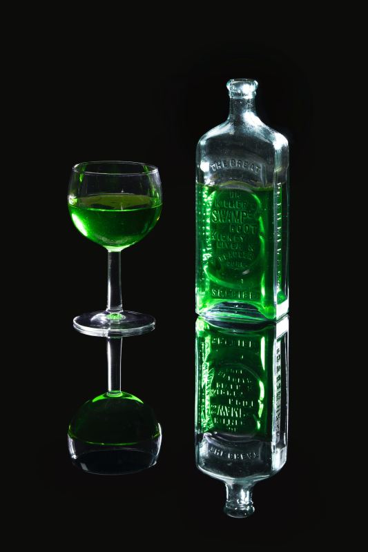 Absinthe in glass next to a bottle with a black background