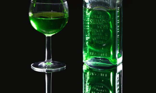Absinthe in glass next to a bottle with a black background
