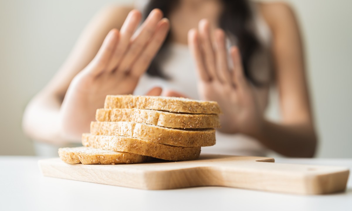 Woman with hands pushed out, refusing to eat white bread slice on chopping board