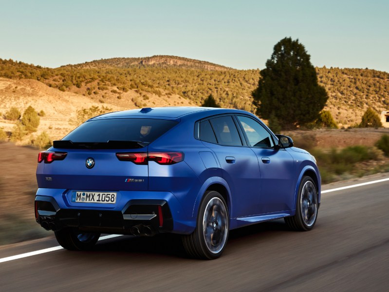 Second generation 2024 BMW X2 compact sports activity coupe right rear three-quarter view driving on a desert highway.