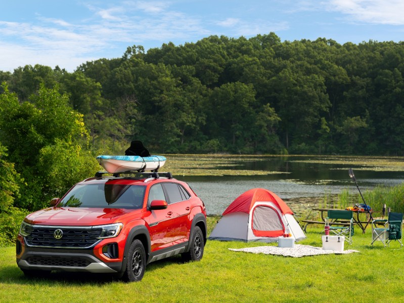 VW Atlas Sport 2-row SUV with Basecamp styling accessories with a kayak on a roof rack parked near a tent beside a lake