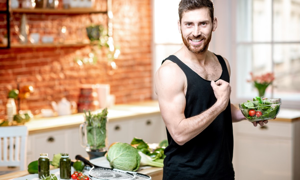 Man showing muscles, eating healthy vegetarian salad