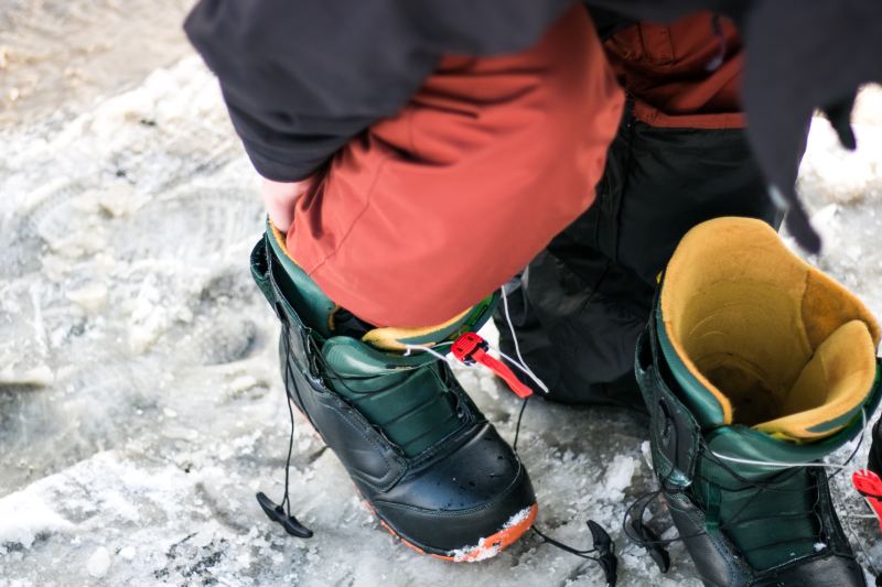 A man puts on a pair of snowboard boots in the parking lot.