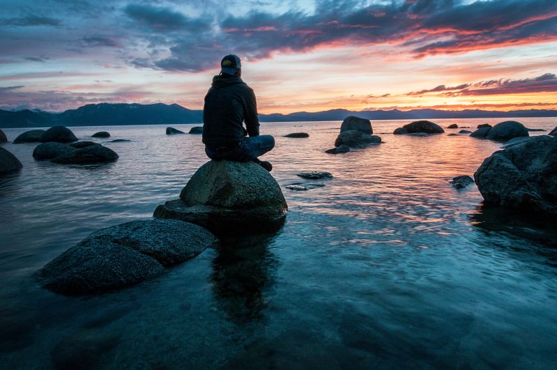 Silhouette man sitting meditating on rock by the ocean