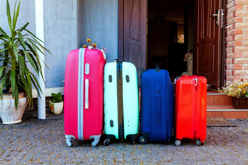Four multicolored suitcases stand in front of the house. luggage near the family car ready for the holidays trip.