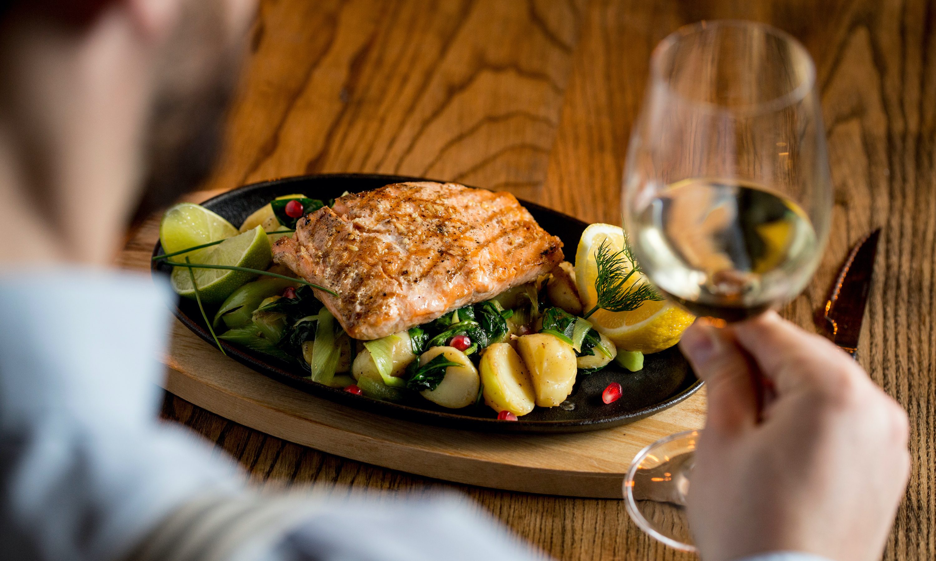 Young man eating salmon fillet with gratinated potatoes, leek and spinach in the restaurant with glass of white wine