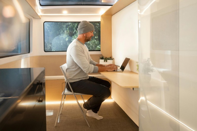 Young man working at the convertible desk inside the Pebble Life electric travel trailer.