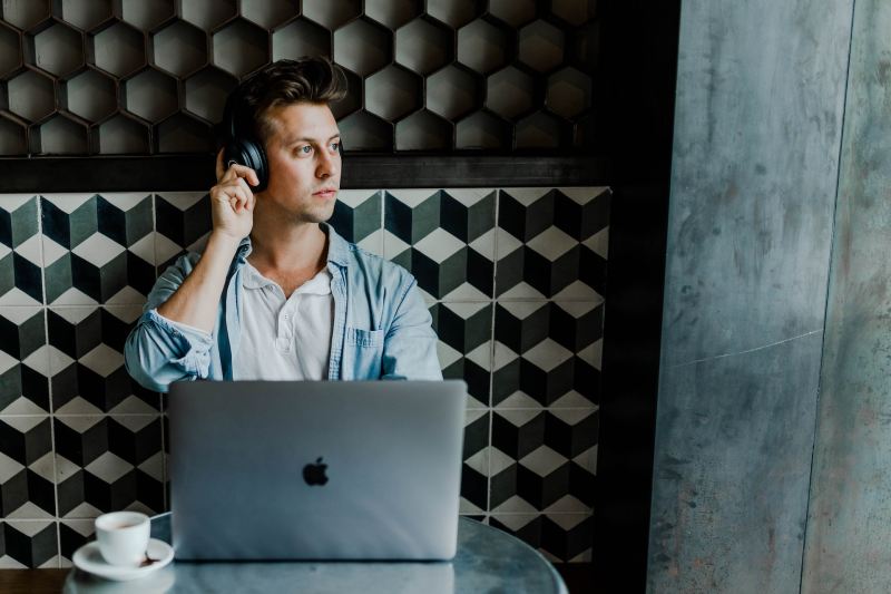 A person looking out the window while wearing headphones and working on a laptop.