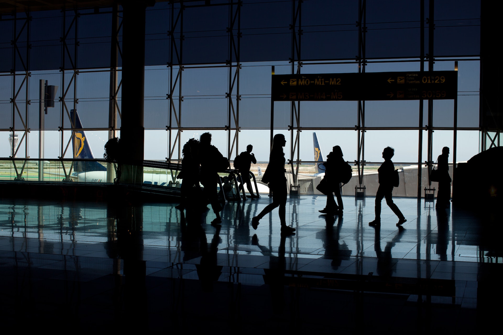 People walking through an airport with large windows in the background