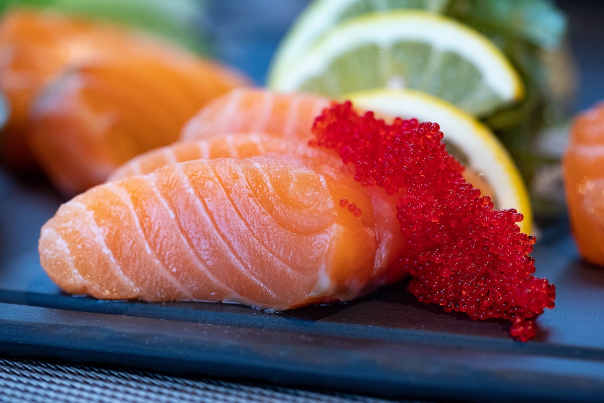 a plate of salmon with red garnish and limes in background