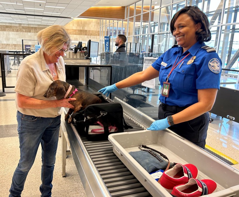 A woman getting her dog out of the carrier at airport security.