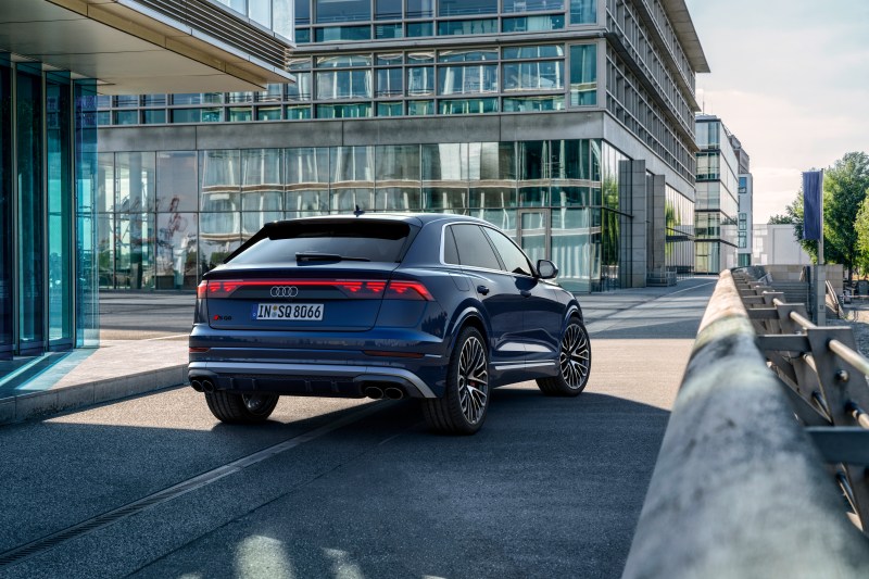 2024 Audi S Q8 in Waitomo Blue right rear three-quarter view in a city roadway between commercial buildings - European Model Shown.