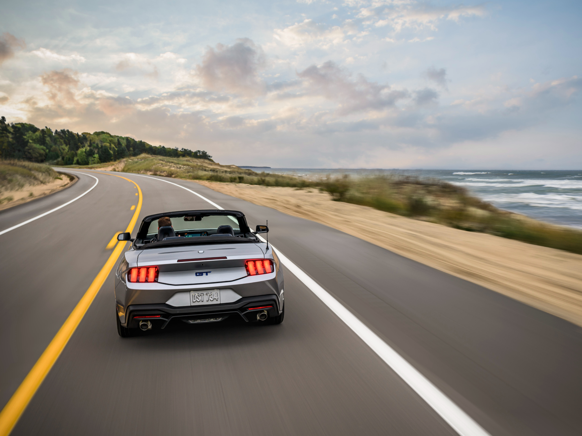 2024 Ford Mustang GT California Special convertible rear view as it drives down the road next to the beach on the right.
