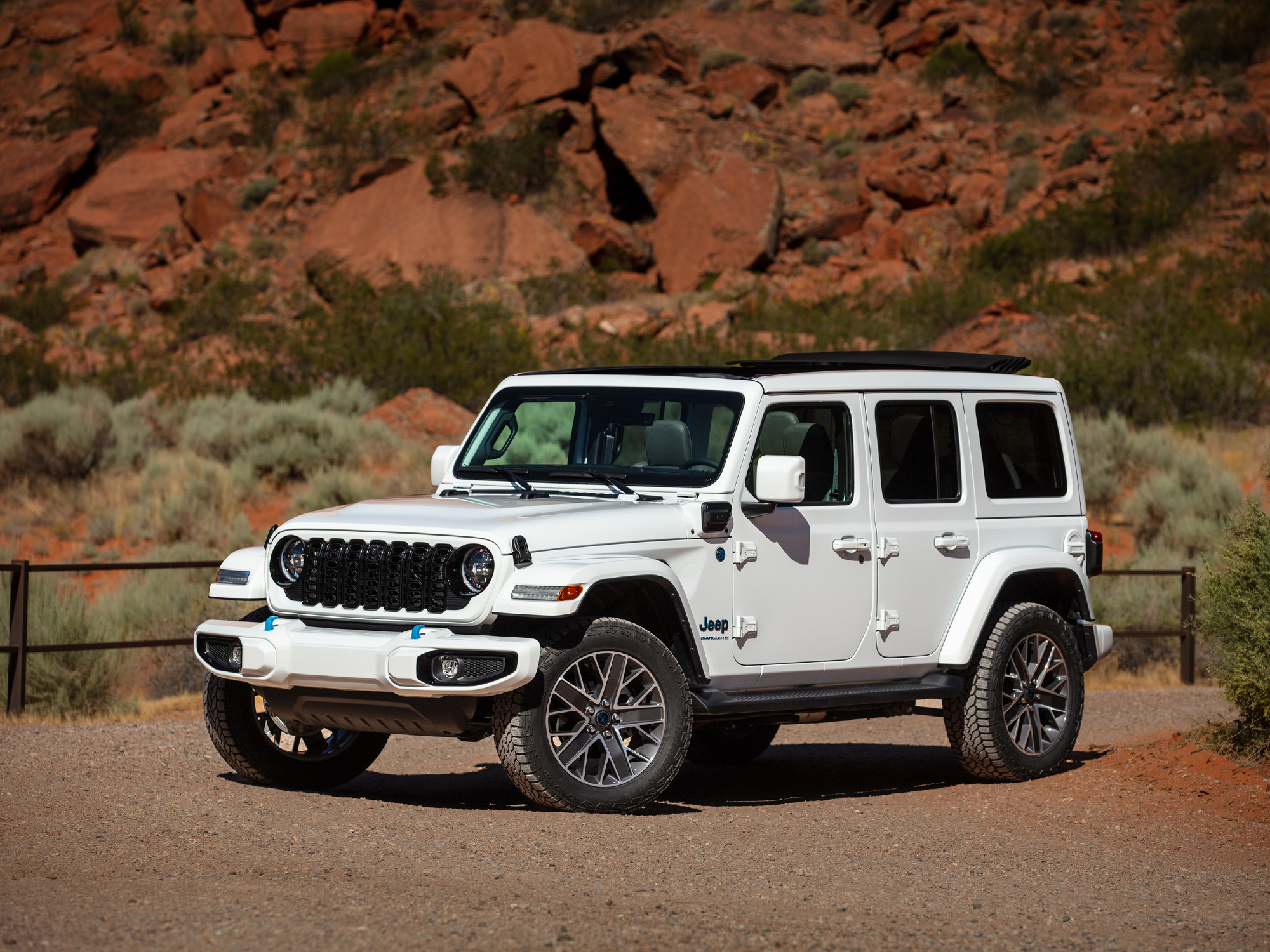 2024 Jeep Wrangler High Altitude 4xe parked in a fenced lot in Springdale, Utah with mountains in the background.