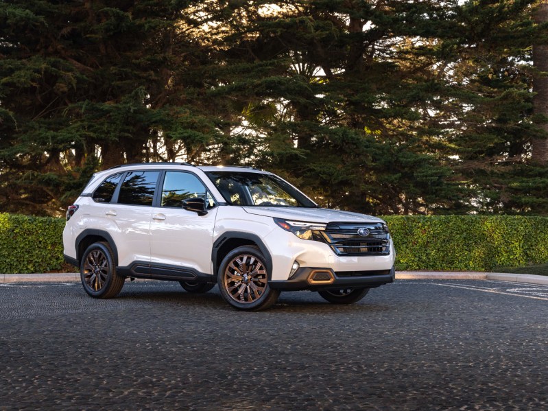 2025 Subaru Forester front right three-quarter view parked on pavement with trees in the background.