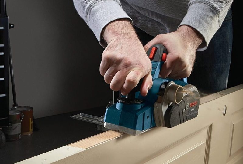 A depiction of a man using a Bosch Woodworking Hand Planer on the side of a door.
