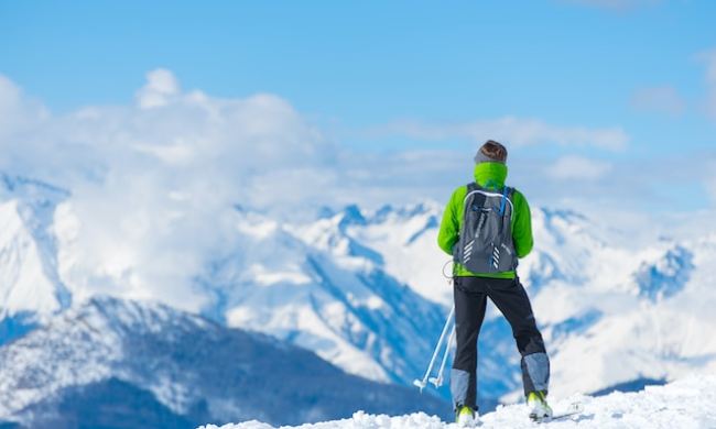 Man standing on a snowy hill trail taking in the view while cross country skiing
