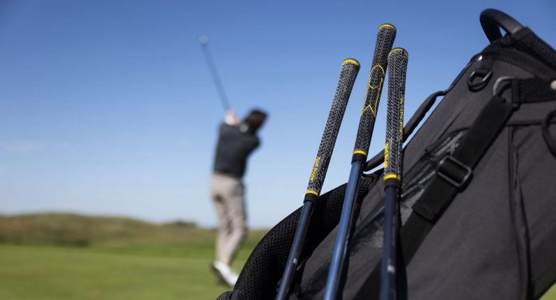 Man hitting a golf ball behind a bag of clubs