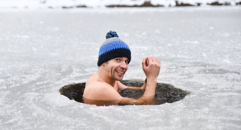 Man in ice water smiling with a beanie on his head