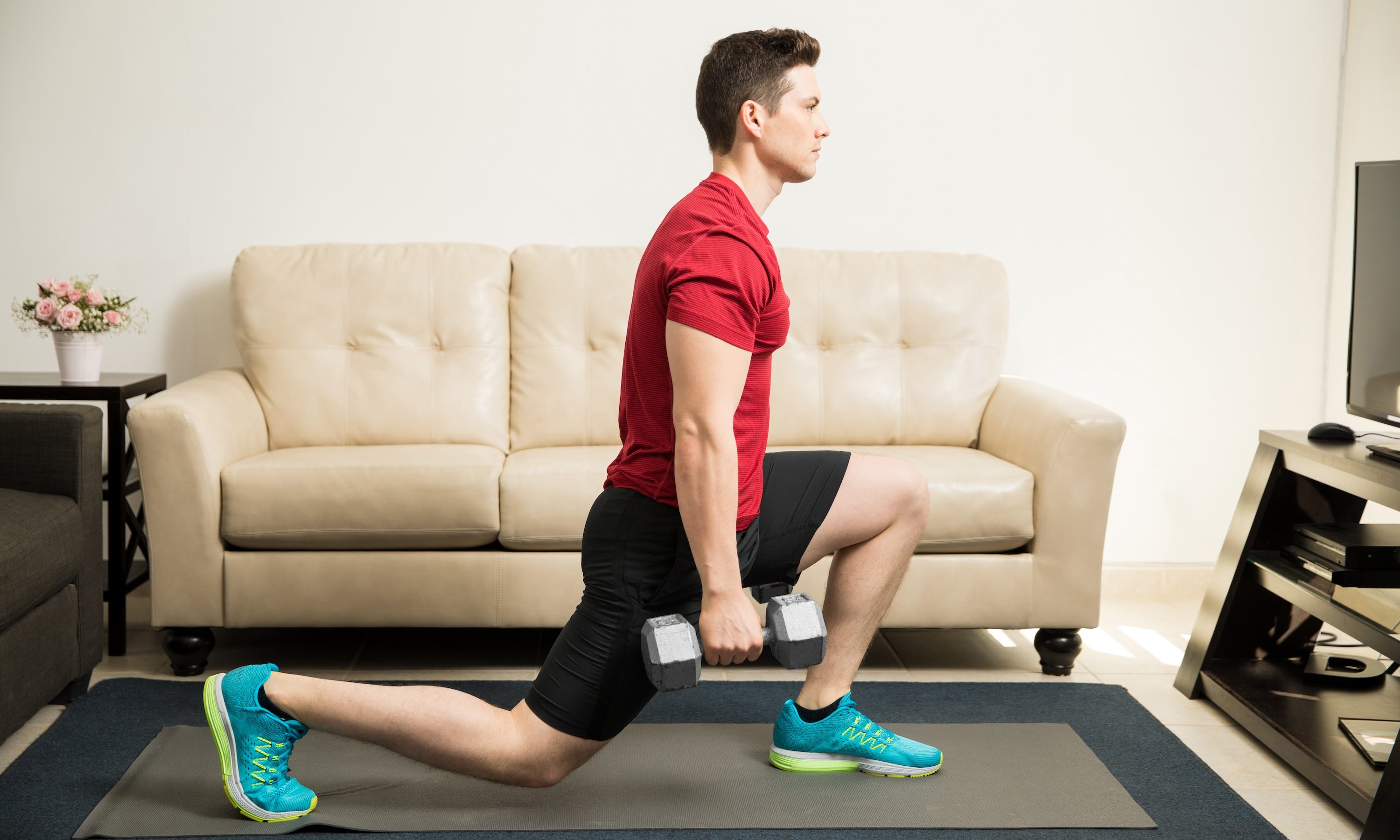 Profile view of a man lunge red shirt young and fit man doing kneeling lunges with a pair of dumbbells at home