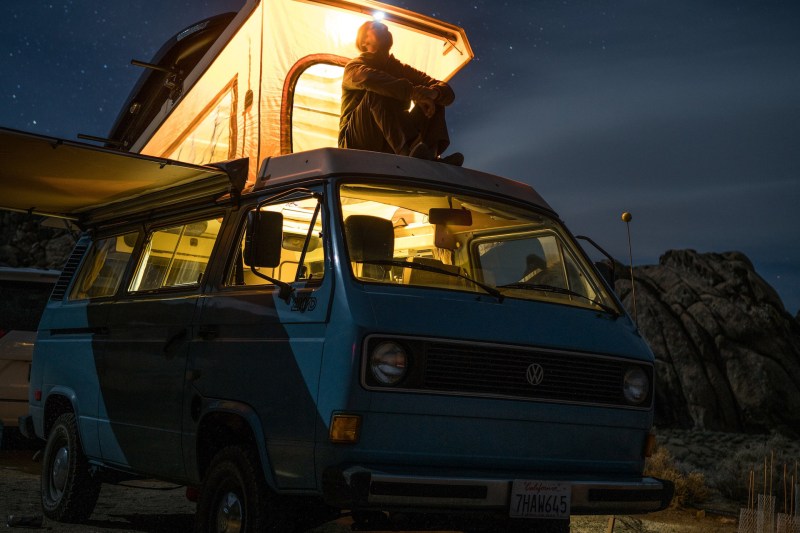 Man sitting atop a campervan with a headlamp at night.