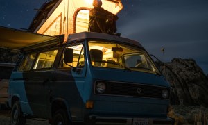 Man sitting atop a campervan with a headlamp at night.
