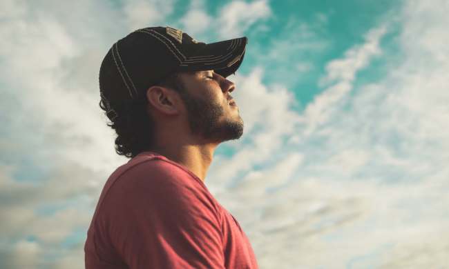 a man in a baseball cap taking a deep breath looking at the sky