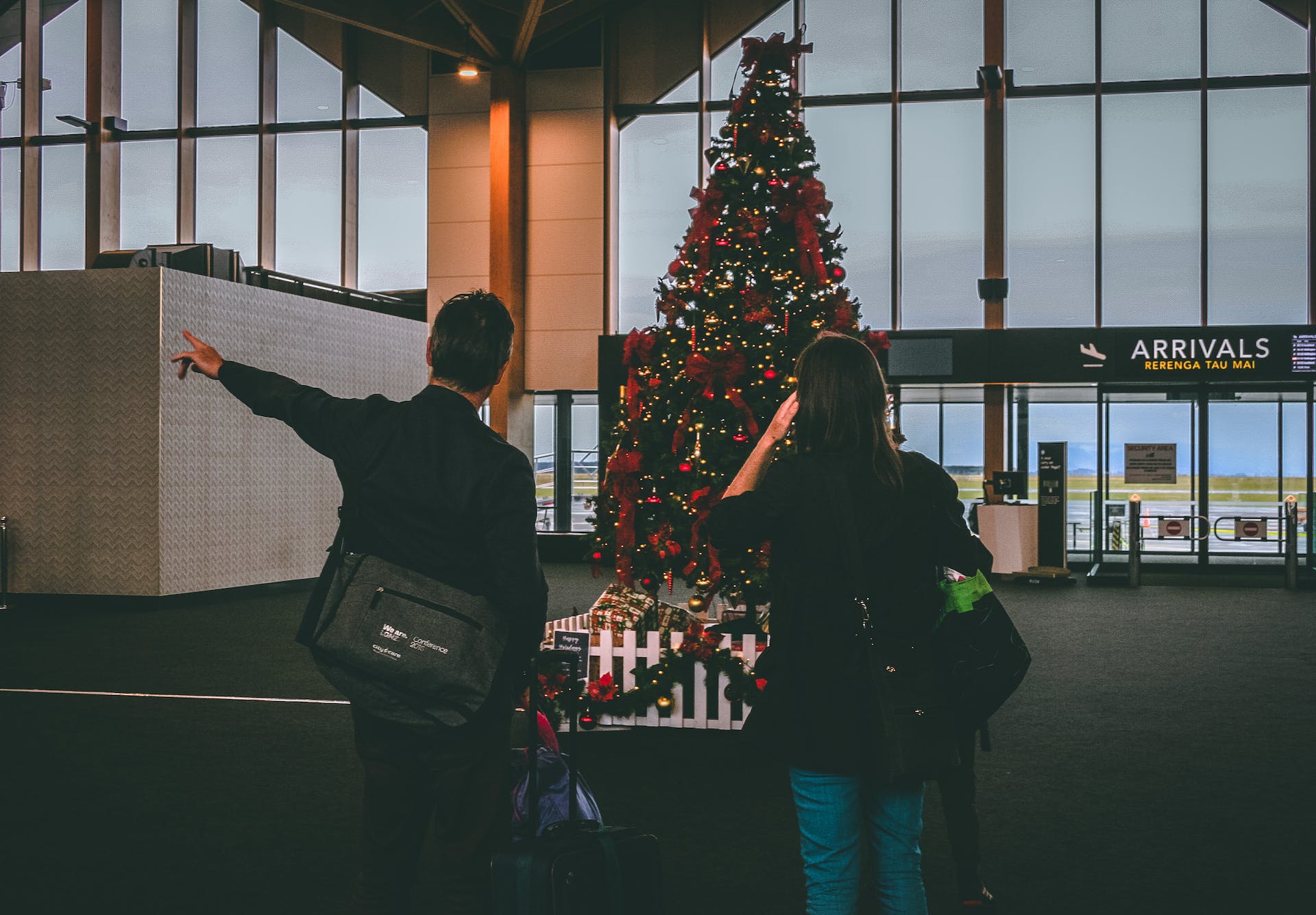 A man and woman inside of an airport stand in front of a christmas tree