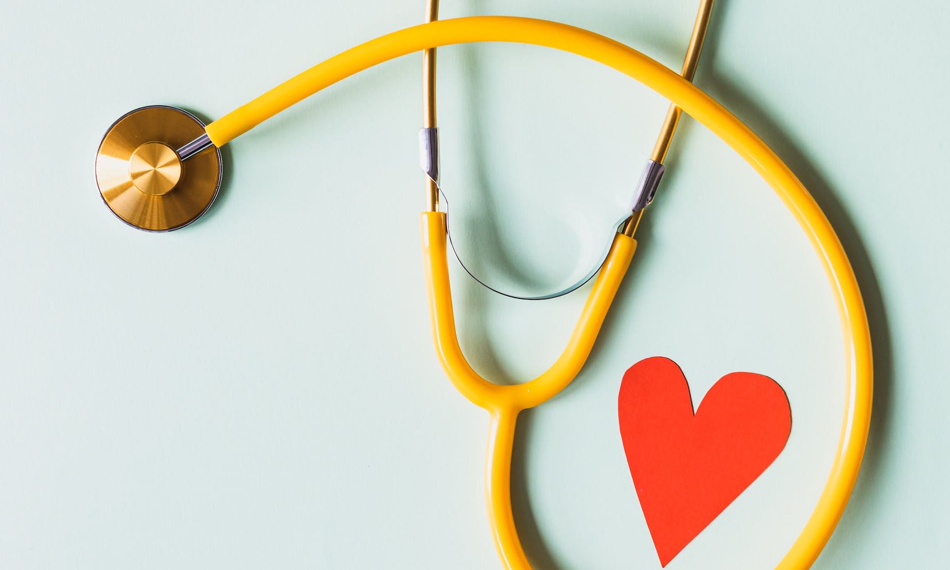 Stethoscope wrapped around a small paper red heart on a light blue background