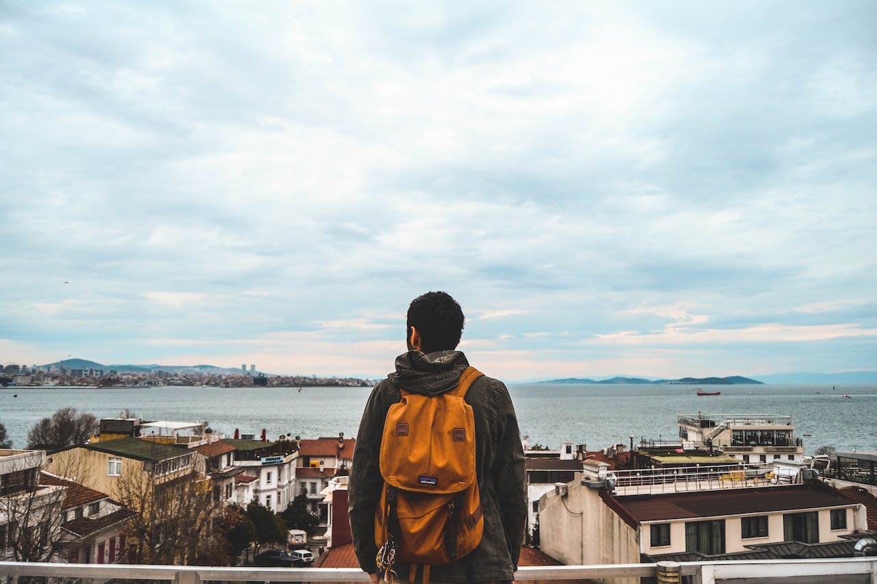 A man pictured from behind wearing a backpack and looking out over the coast in Turkey