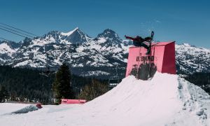 A snowboarder hits a park feature on their freestyle snowboard.