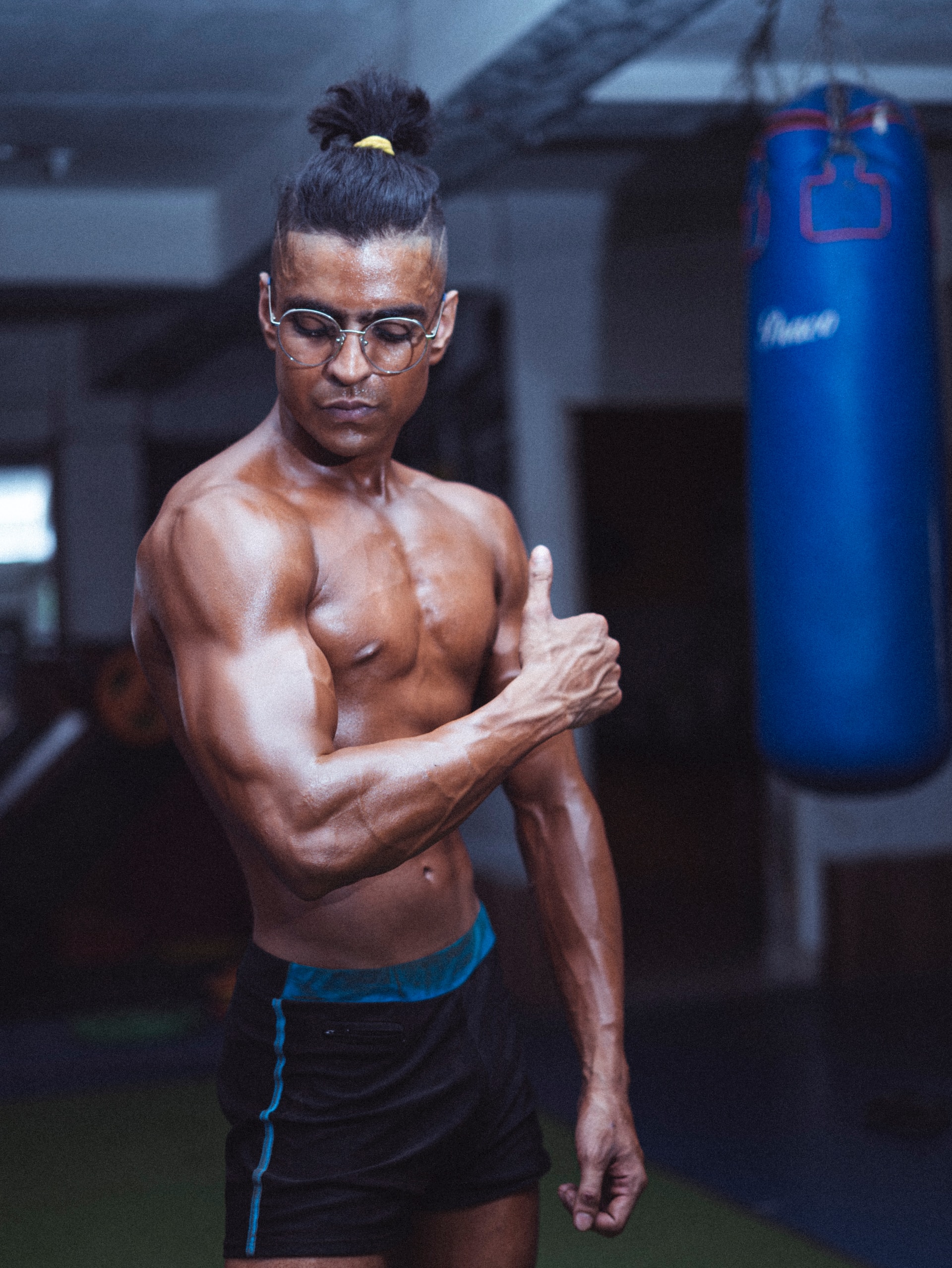 Man with no shirt flexing in gym near boxing punch bag