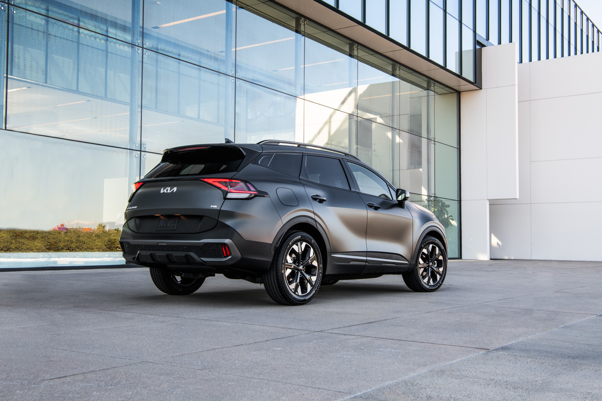 2024 Kia Sportage PHEV right rear three-quarter view parked in front of a modern office building.