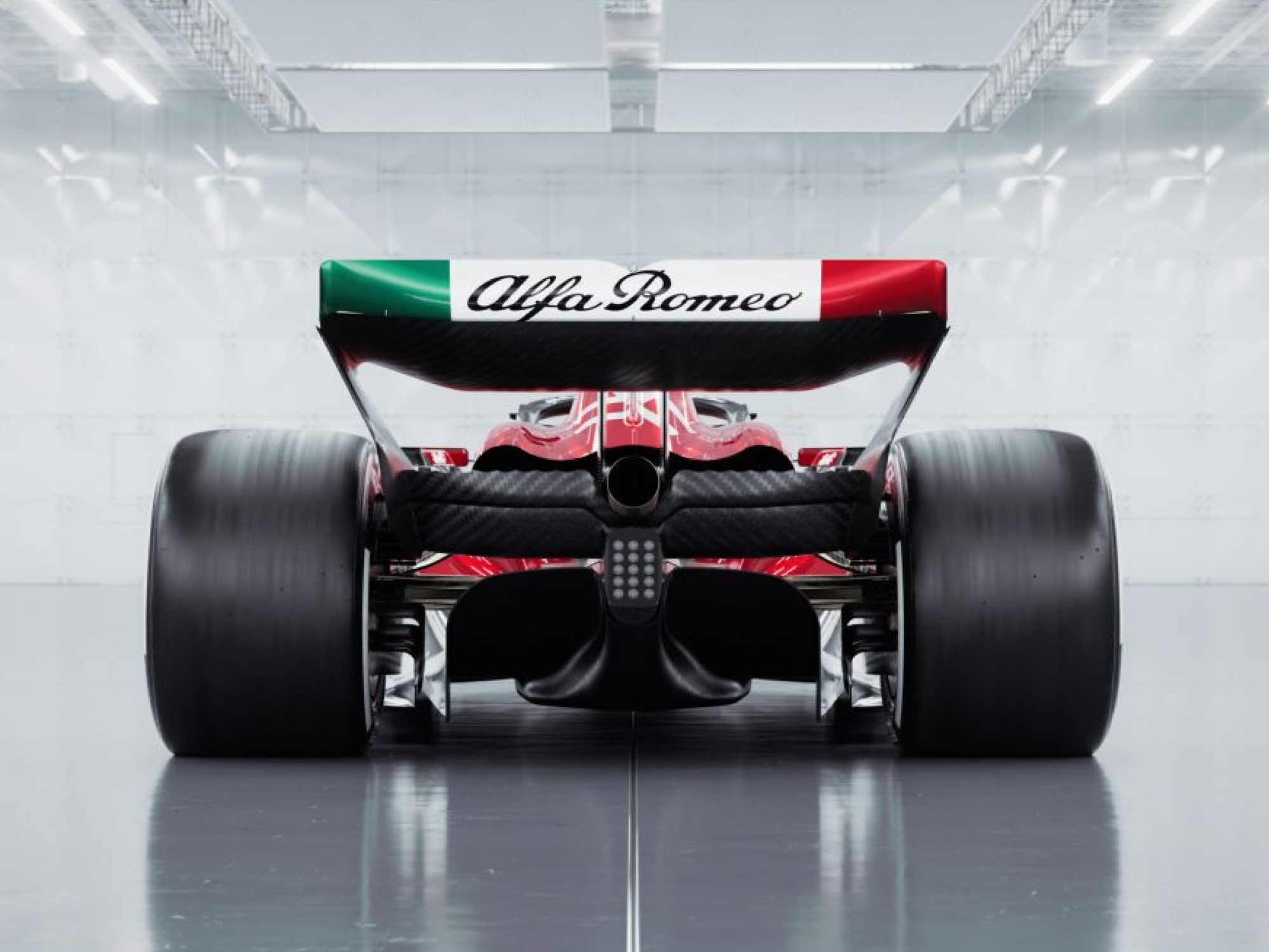 Vista trasera del coche de carreras de Fórmula 1 de la última temporada 2023 de Alfa Romeo sobre un fondo plateado que parece ser un garaje del pit lane de carreras de F1.