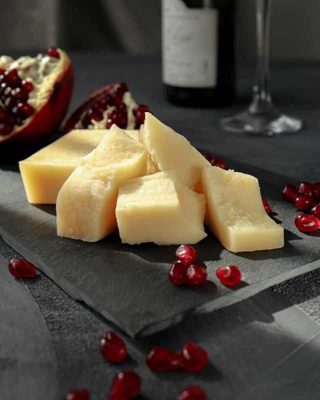 Cheese sliced on black cutting board and table with red grapes and dark background
