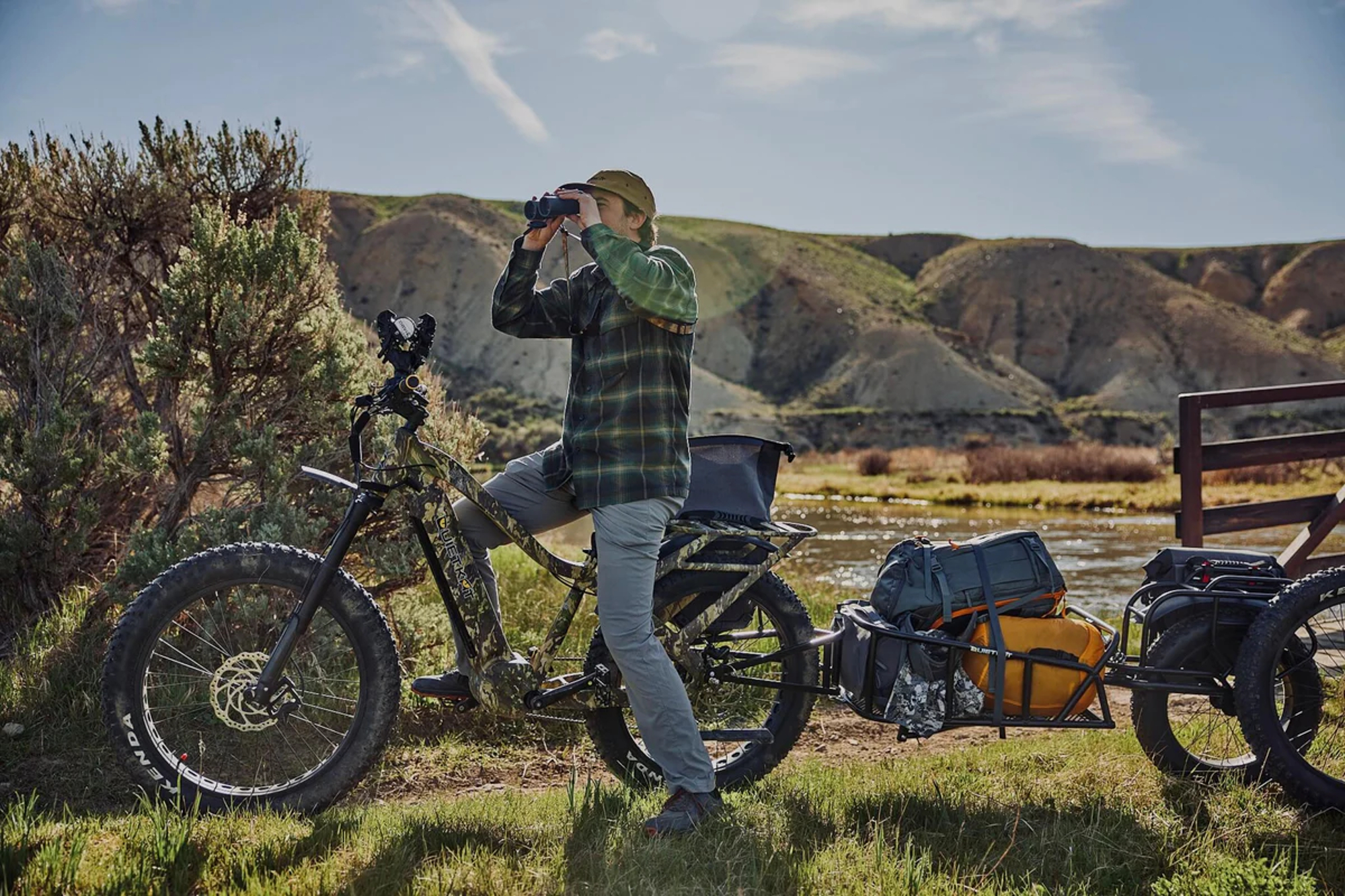 Rider looking through binoculars seated on a QuietKat All Terrain e-bike with a trailer.