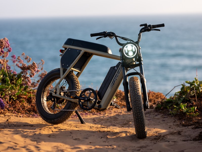 Right front three-quarter view of a Juiced Bikes Scrambler X2 parked on sand with ocean in the background.
