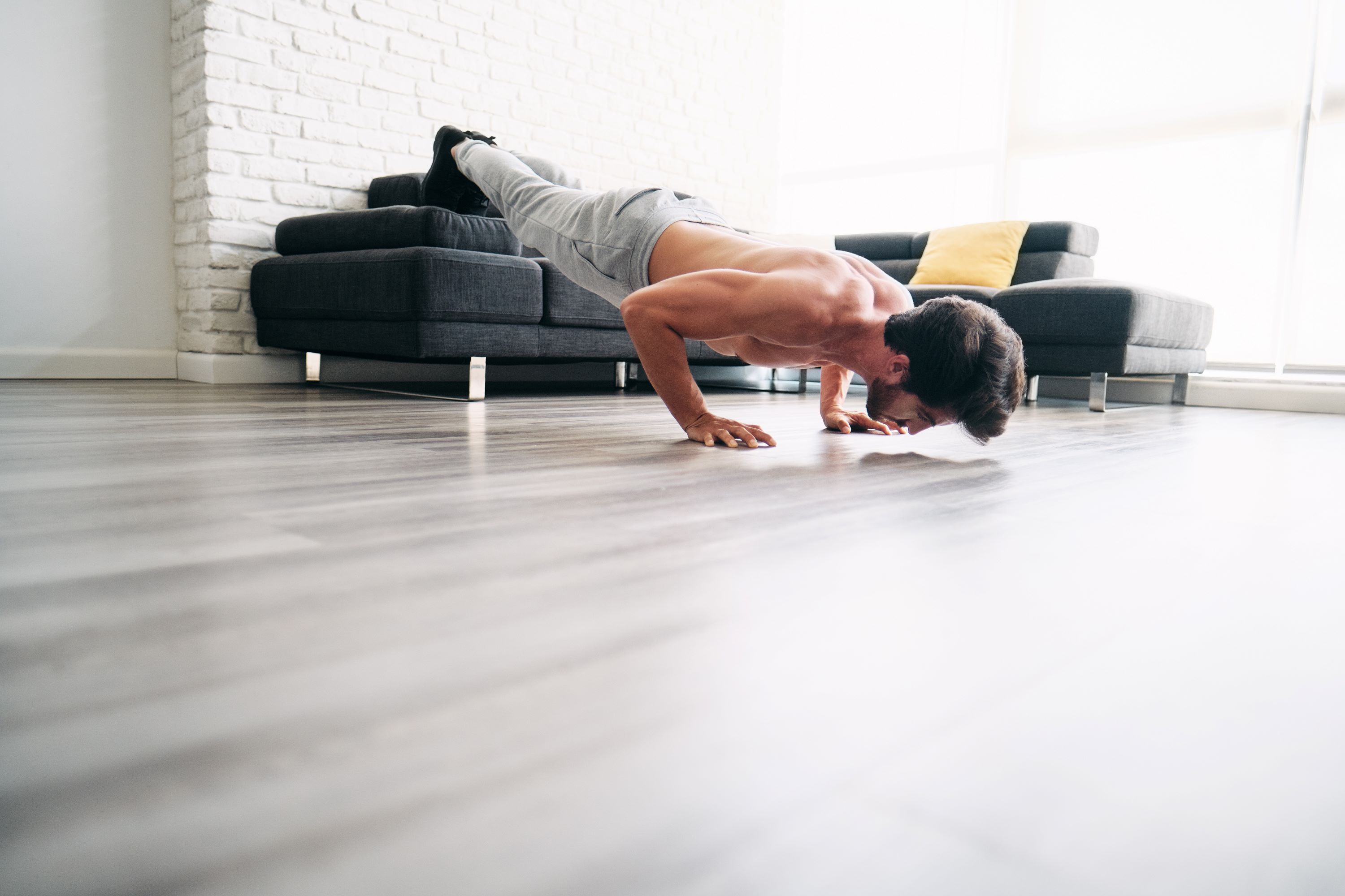 man exercising balancing plank type pose on couch at home wearing sweatpants