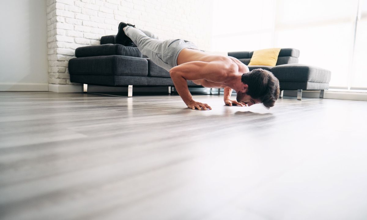 Man exercising balancing plank type pose on couch at home wearing sweatpants