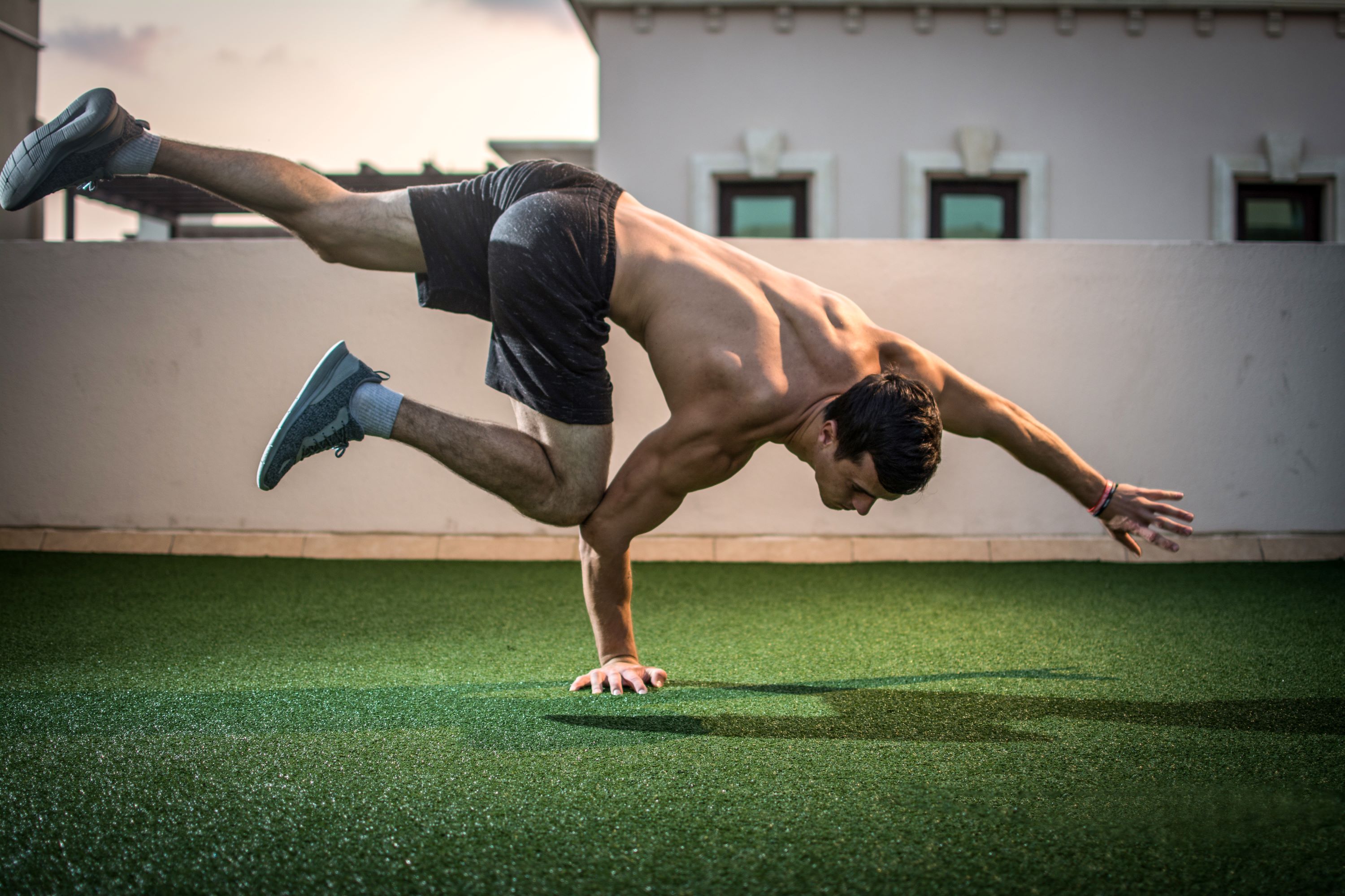 man balancing on hand exercising wearing shorts no shirt on grass outside