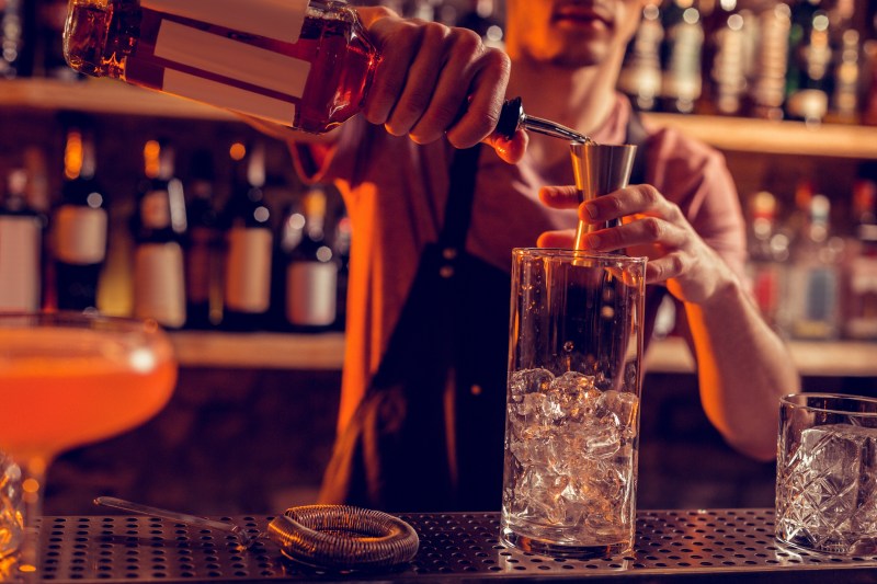 Pouring alcohol. Barman working at night and wearing uniform pouring alcohol into glass with ice