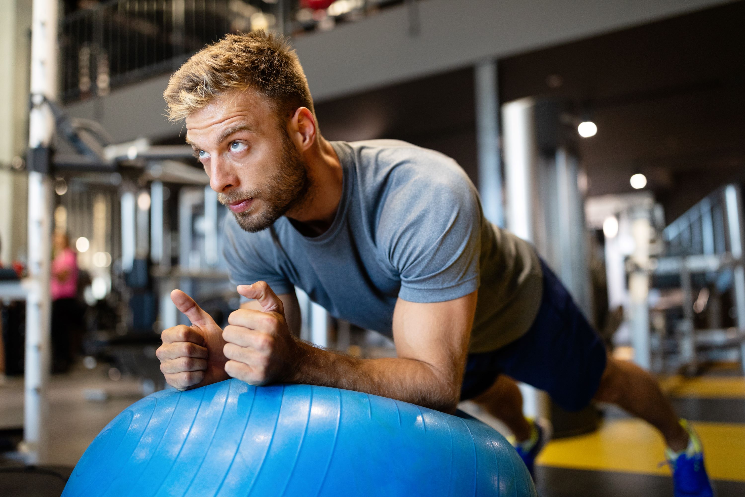 blonde guy on yoga or pilates ball doing pilates exercise and stretch on wooden floor