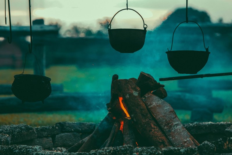 A smoldering campfire heating up an iron pot in the dusk