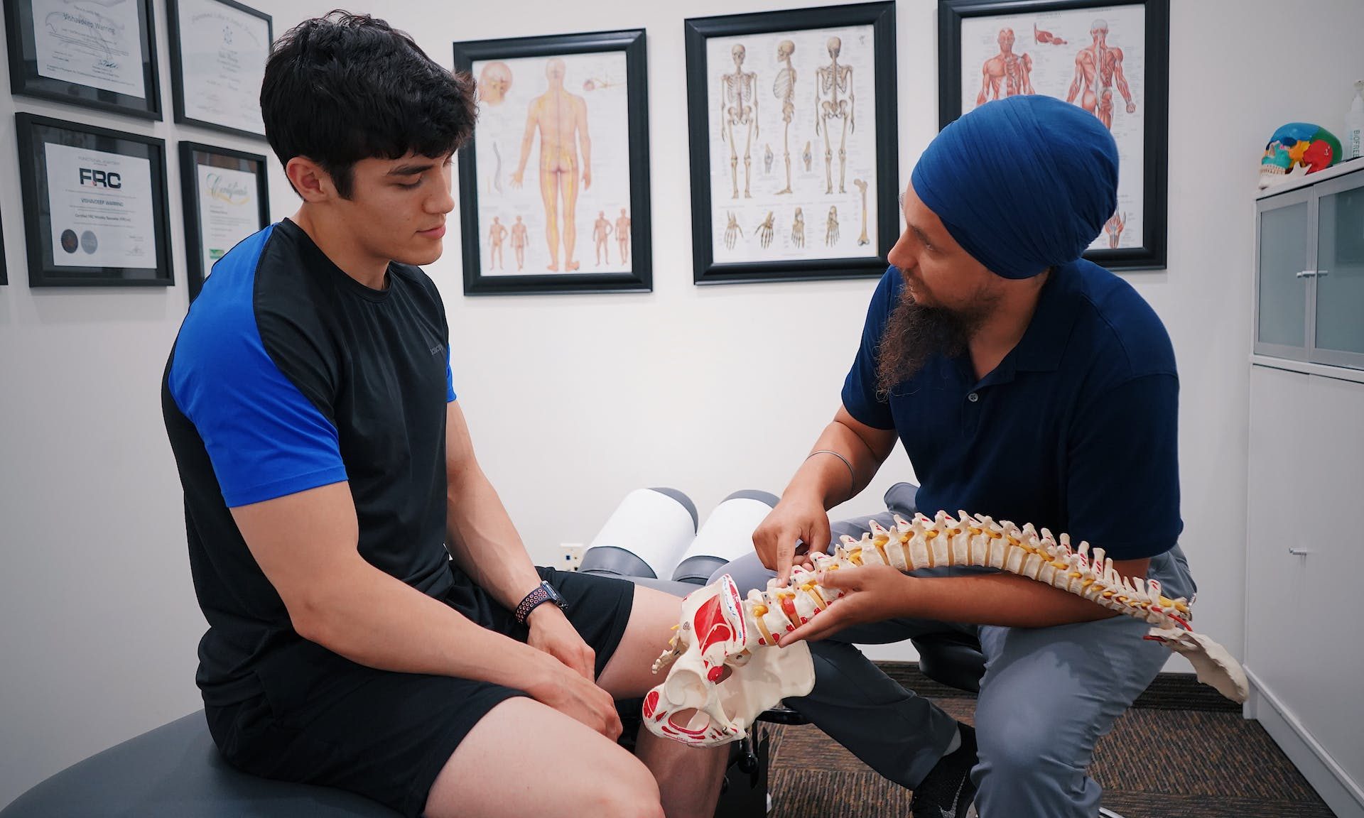 Doctor or healthcare professional discussing bone health and showing model of spine to patient sitting on bed in office