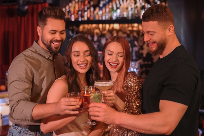 Happy friends clinking glasses with fresh cocktails in bar