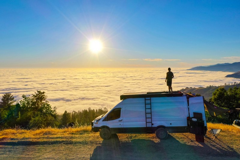 Man standing atop a conversion van looking out at Big Sur, California.