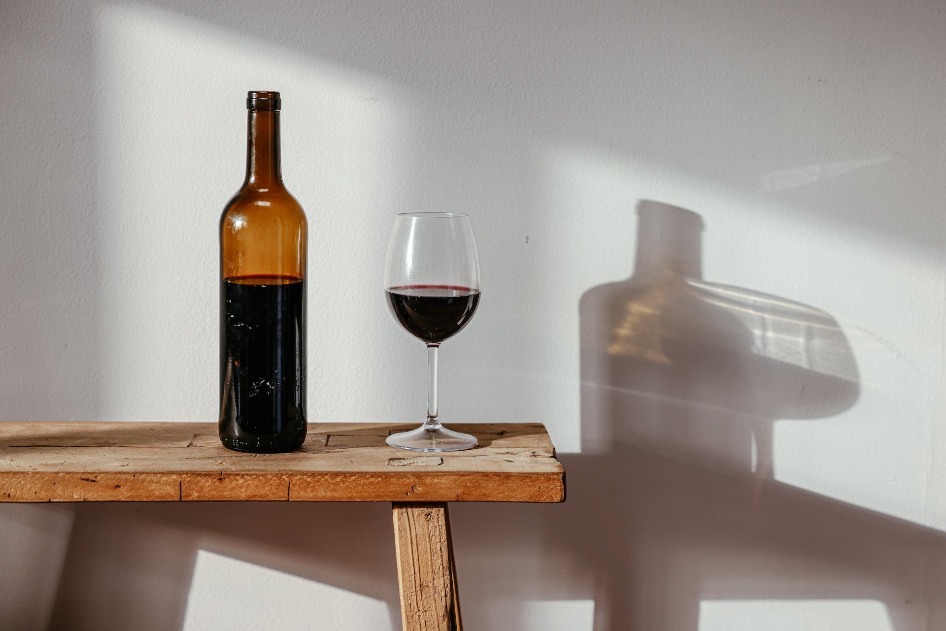 Bottle and glass of red wine on bench