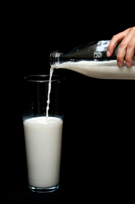 Pouring milk from a glass bottle into a glass with a black background